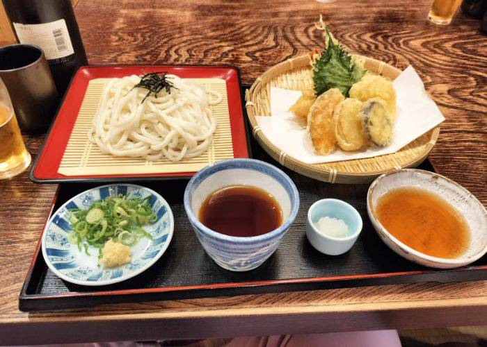 A set meal at Oshokuji Dokoro Asuka, featuring tempura, udon noodles, dipping sauces and more.